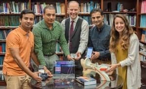 From left: Research assistant Nursadul Mamun, teaching assistant Ram Charan Chandra Shekar, Dr. John Hansen, senior research scientist Hussnain Ali and research assistant Juliana Saba show off the tools in their CCi-MOBILE project. The CCi-MOBILE research interface, held by Hansen, connects to microphones, which a user of a cochlear implant or hearing aid wears to collect audio. The data is processed with algorithms on a connected laptop or smartphone. Then, CCi-MOBILE sends the processed audio through another connection to the user’s cochlear implant or hearing aid.